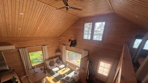 A cabin interior with a high ceiling, wooden walls, a dining area, a sofa set, and a view of the outdoors. - Vrbo Property (pello)