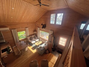A cabin interior with a high ceiling, wooden walls, a dining area, a sofa set, and a view of the outdoors. - Vrbo Property (pello)