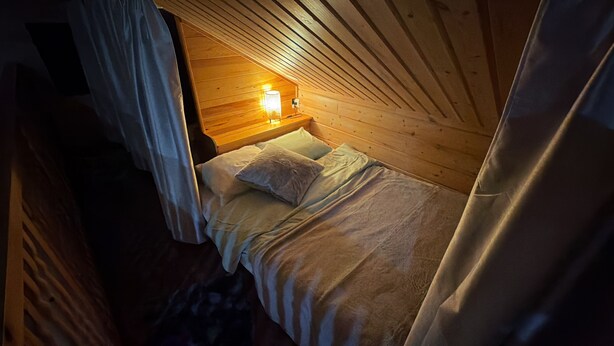A cozy room with a bed, a nightstand with a lamp, and wooden walls. - Vrbo Property (pello)