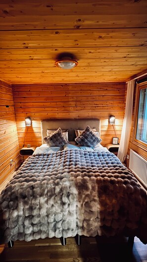 Un dormitorio de cabaña de madera con una cama, dos lámparas de noche y una ventana.
