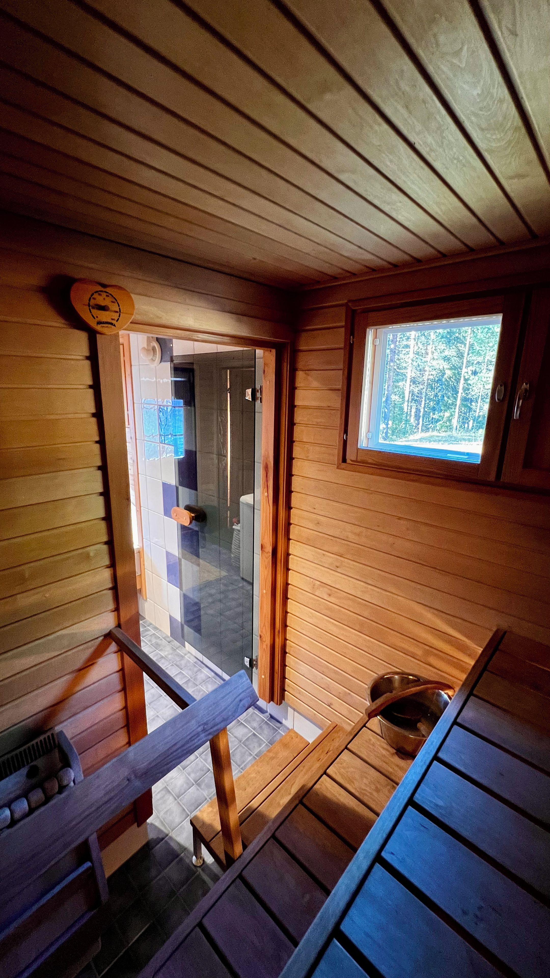 A wooden cabin interior with a wooden bench, a window, and a door leading outside.