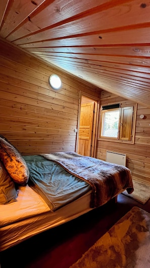 A wooden cabin room with a bed, a window, and a door.