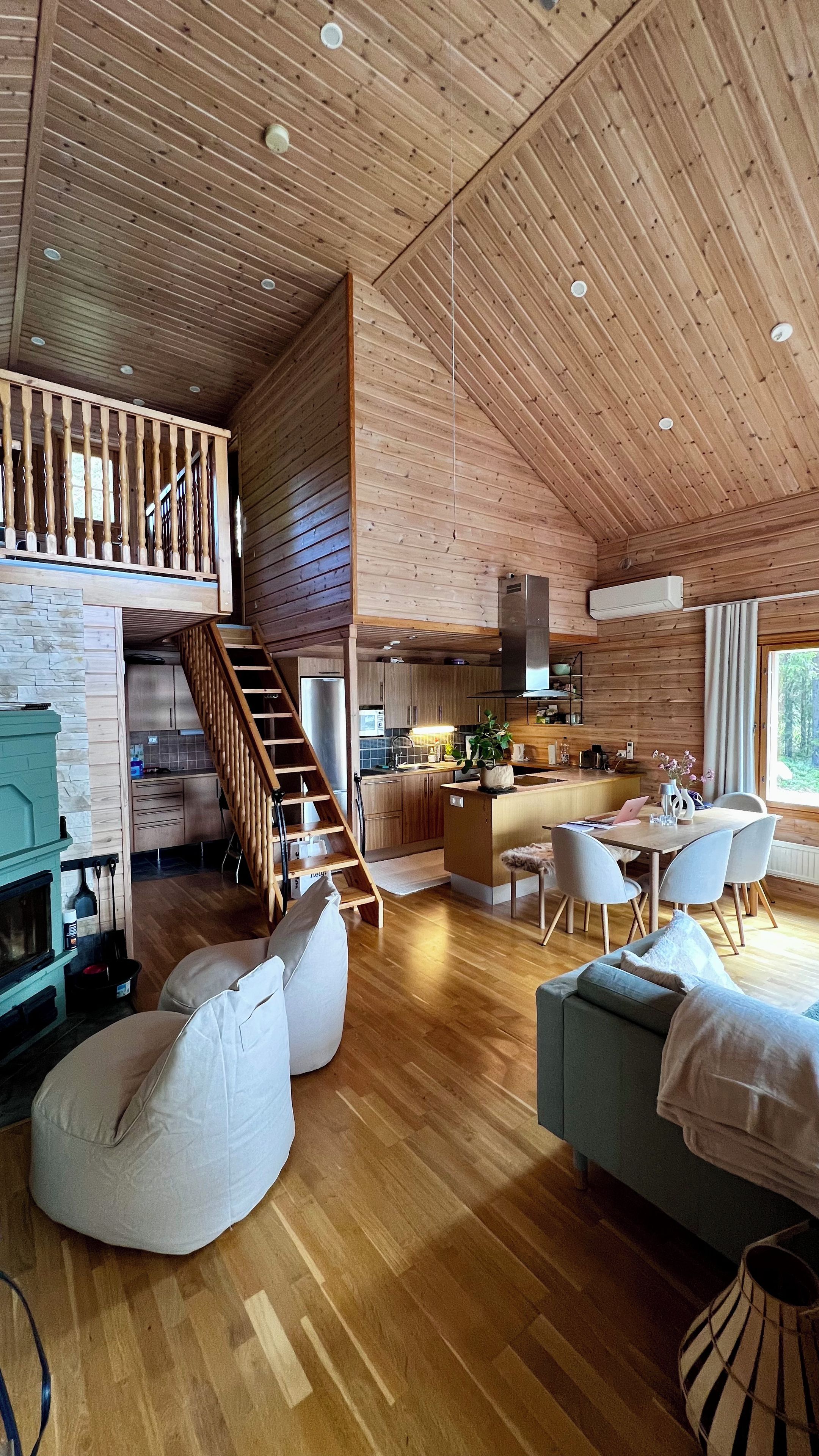 A spacious living area with a wooden ceiling, a kitchen, a dining area, and a staircase leading to an upper level.