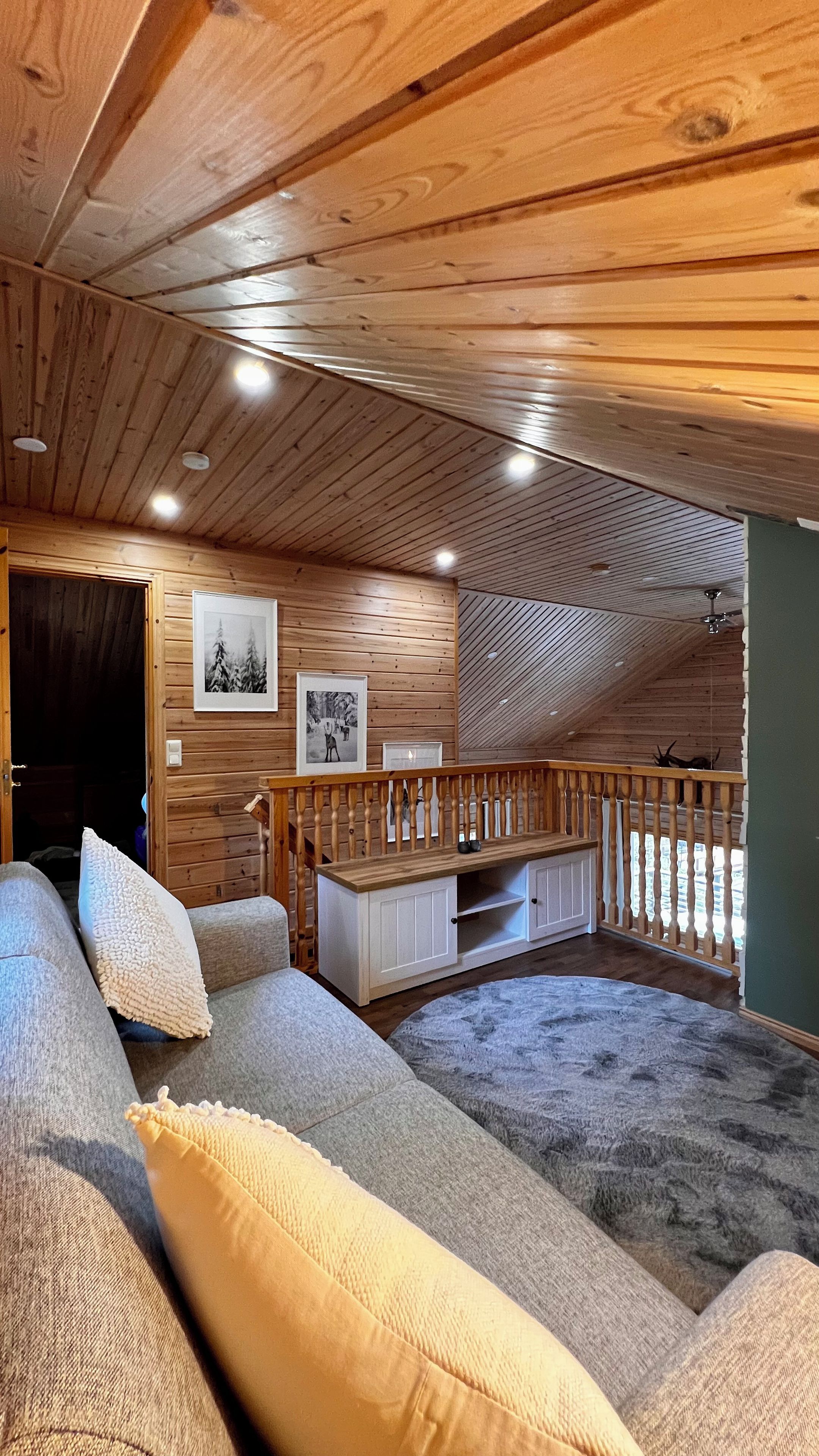 A cozy cabin interior with a wooden ceiling, a sofa with cushions, a small table, and a picture on the wall.