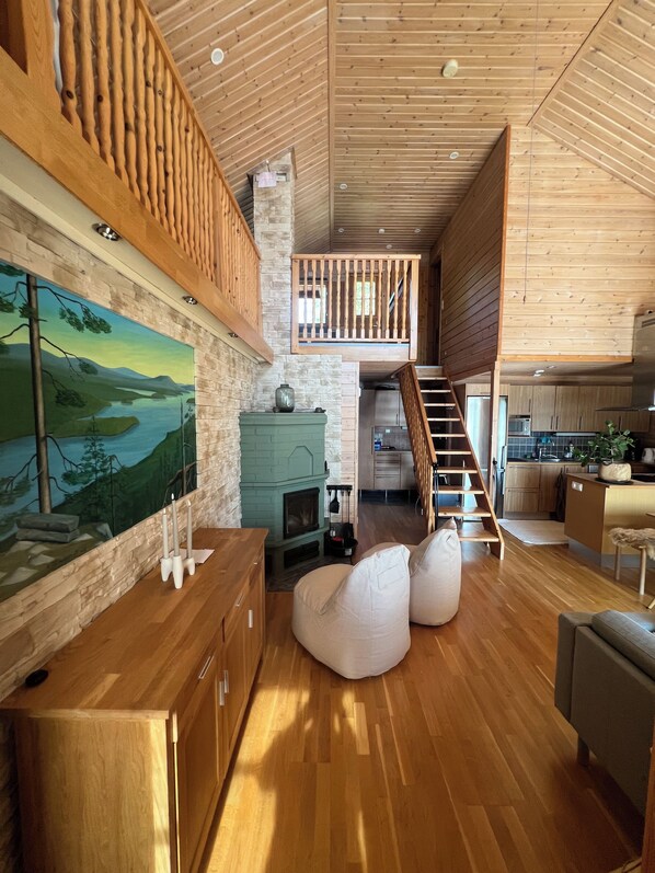 A spacious living area with a wooden floor, a fireplace, a painting, and a kitchen in the background.