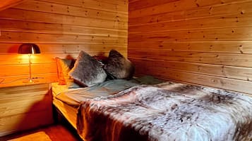 A cozy cabin room with a wooden ceiling, a bed with a blanket, pillows, and a bedside lamp.