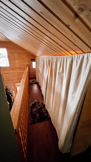Un intérieur en bois avec un plafond en pente, une fenêtre et un rideau.