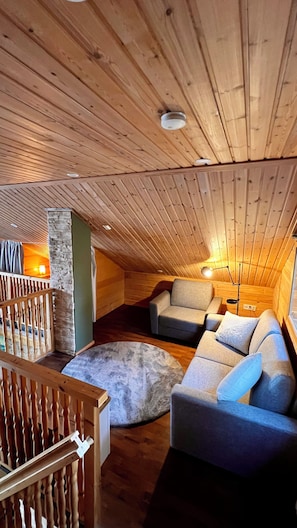 Acogedor dormitorio en ático con vigas de madera, pared de piedra, sofá acolchado y barandilla de madera.