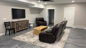 A living room with a flat-screen TV, leather sofa, wooden coffee table, and a ceiling fan. - New 3-bedroom house with AC in charming Mapleton with covered walk-out patio. (Mapleton)