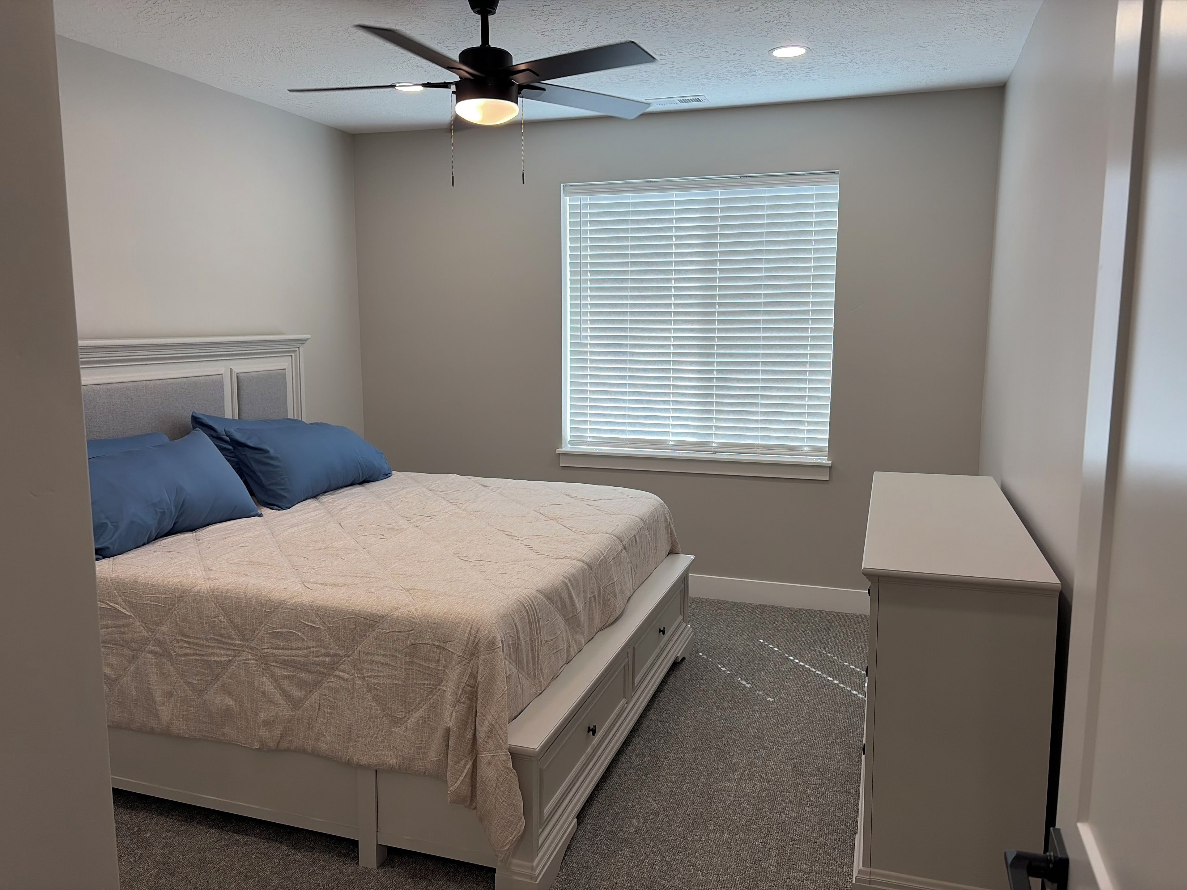 Een slaapkamer met een bed, een plafondventilator, een raam met zonwering en een nachtkastje.