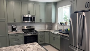 A kitchen with green cabinets, a stainless steel refrigerator, a microwave, and a stove. - New 3-bedroom house with AC in charming Mapleton with covered walk-out patio. (Mapleton)