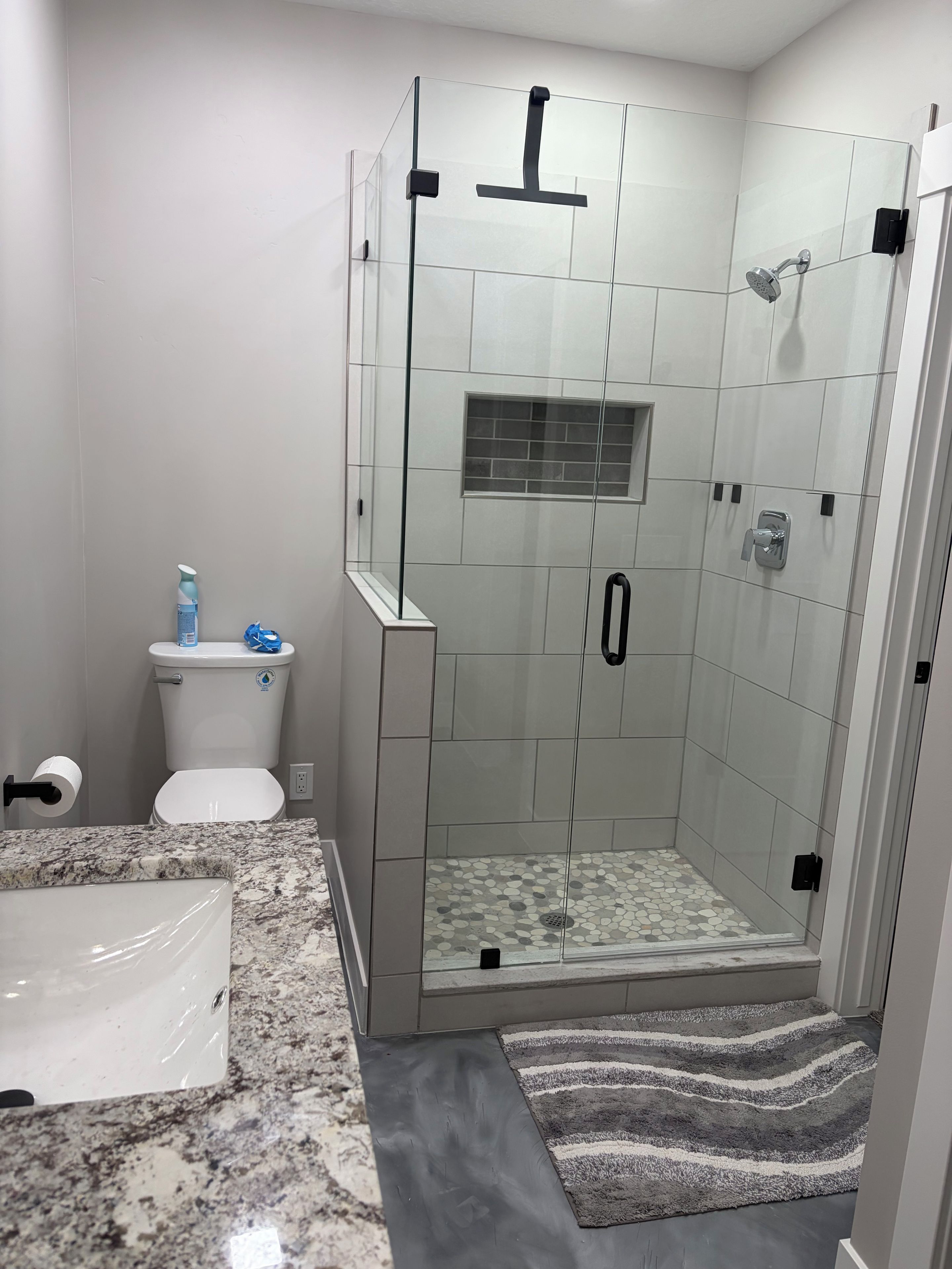 Een moderne badkamer met een douchecabine van glas, een toilet en een granieten aanrechtblad.