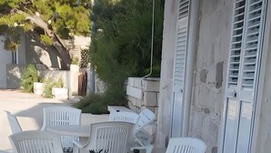 Uma área de pátio com mesa, cadeiras, um banco e um vaso de planta.