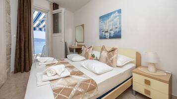 A hotel room with a bed, a bedside table with a lamp, a painting on the wall, and a view of the sea through the window.