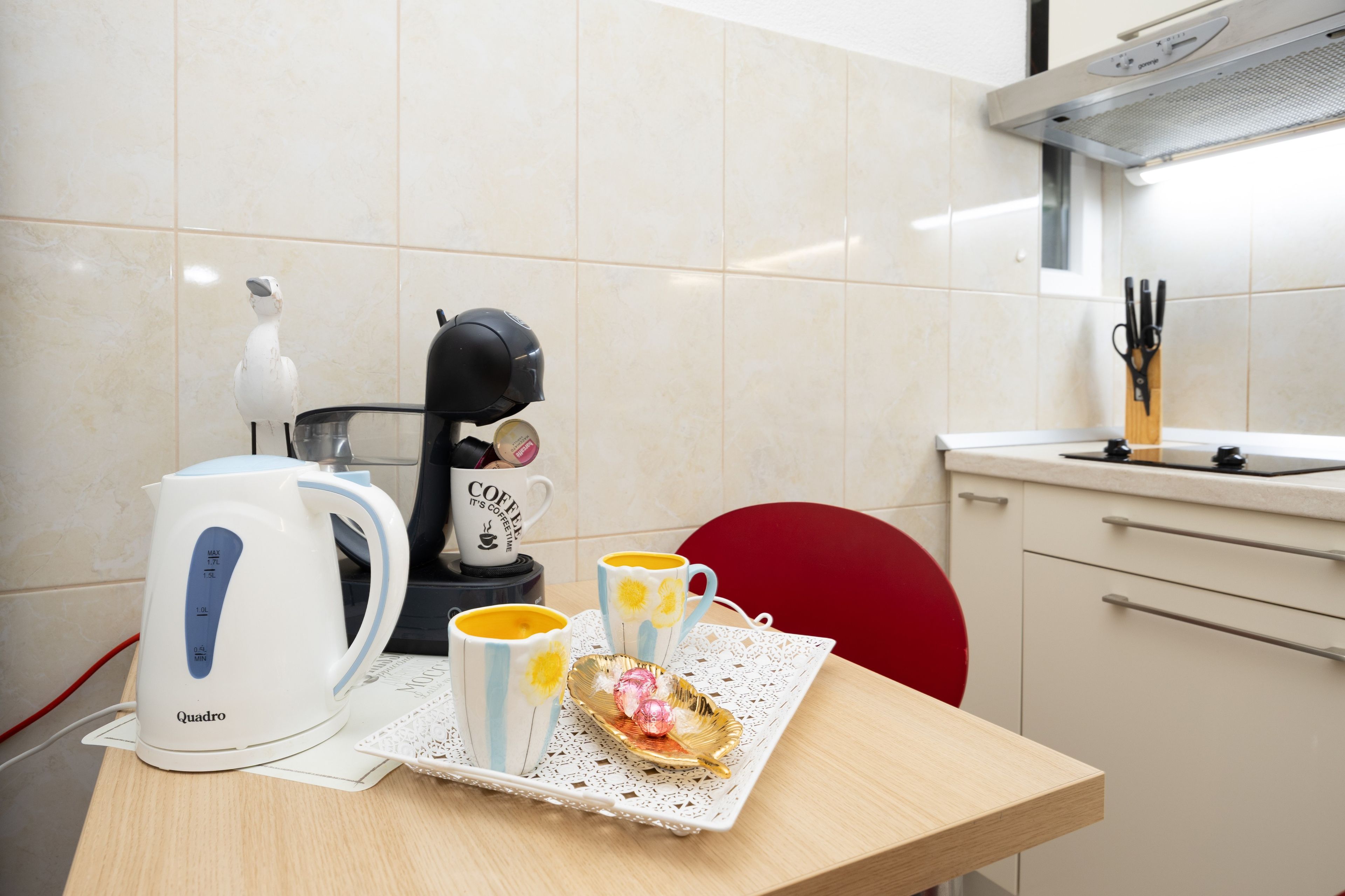 A kitchen with a coffee maker, a kettle, and two mugs on a table.