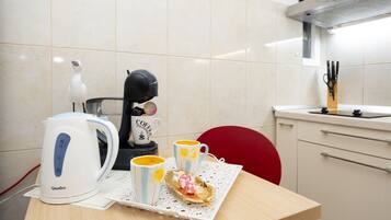 A kitchen with a coffee maker, a kettle, and two mugs on a table.
