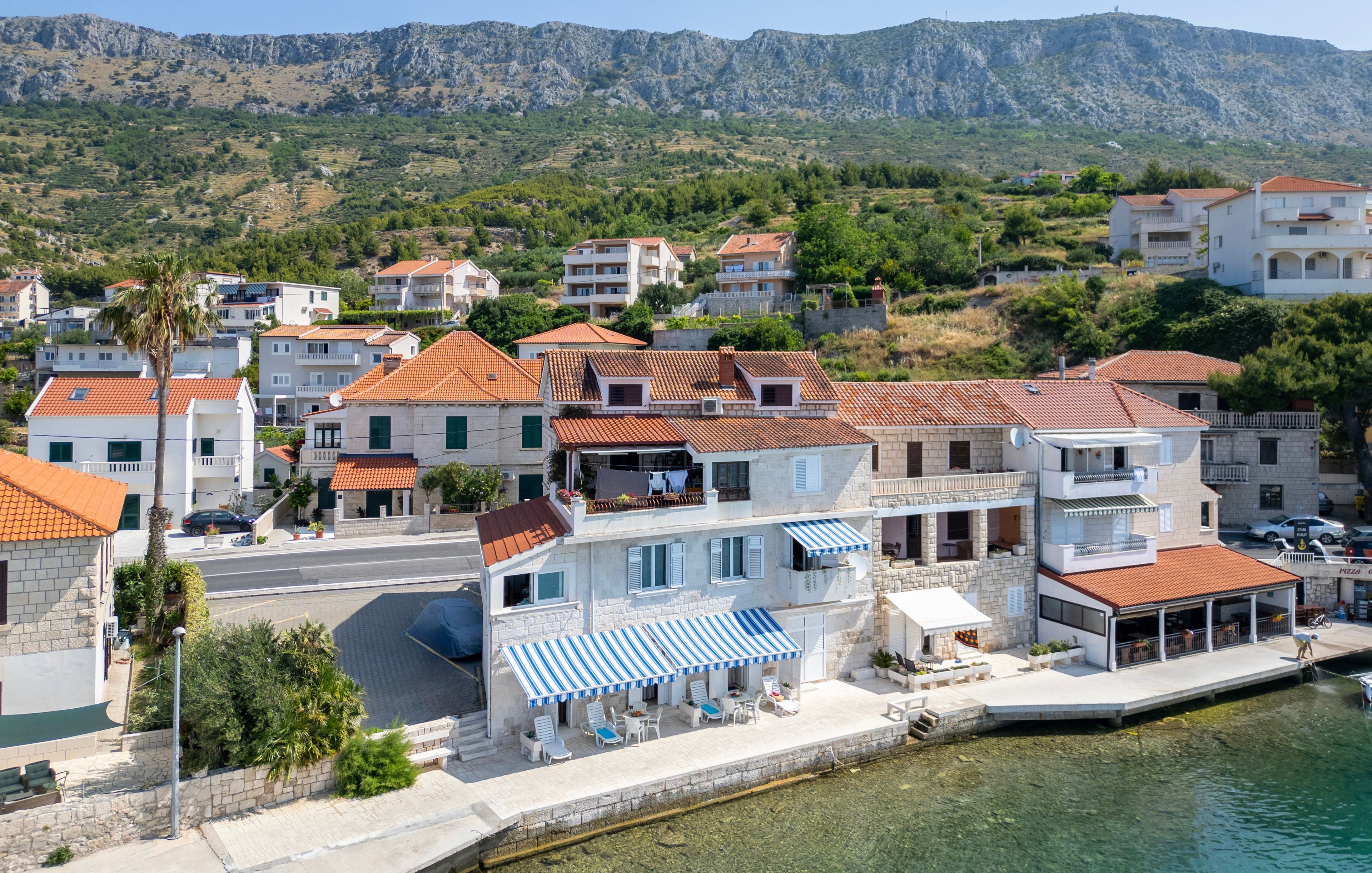 A coastal town with stone buildings, a clear view of the sea, and a paved waterfront area.