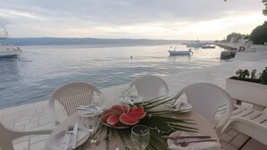 Mesa posta para dois, vista para o mar e barcos ao fundo.