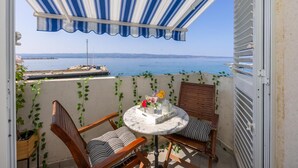 Uma varanda com vista para o mar, uma mesa redonda com um vaso de flores e duas cadeiras de madeira.