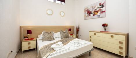 A hotel room with a bed, bedside tables, a dresser, a painting, and a window.