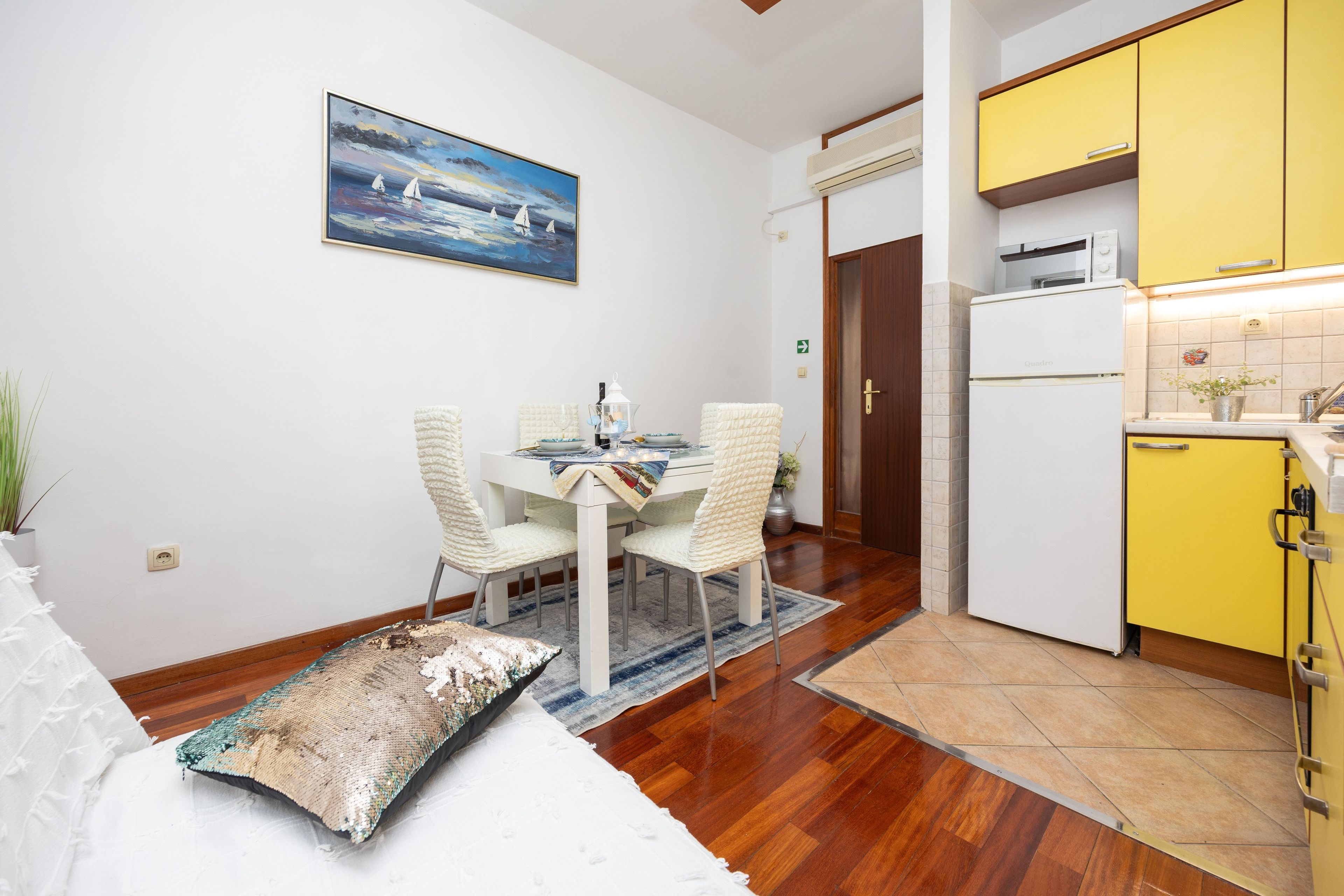 Un comedor con una mesa y sillas, un cuadro en la pared y una cocina con armarios amarillos.