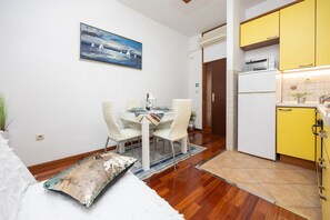 A dining area with a table and chairs, a painting on the wall, and a kitchen with yellow cabinets.