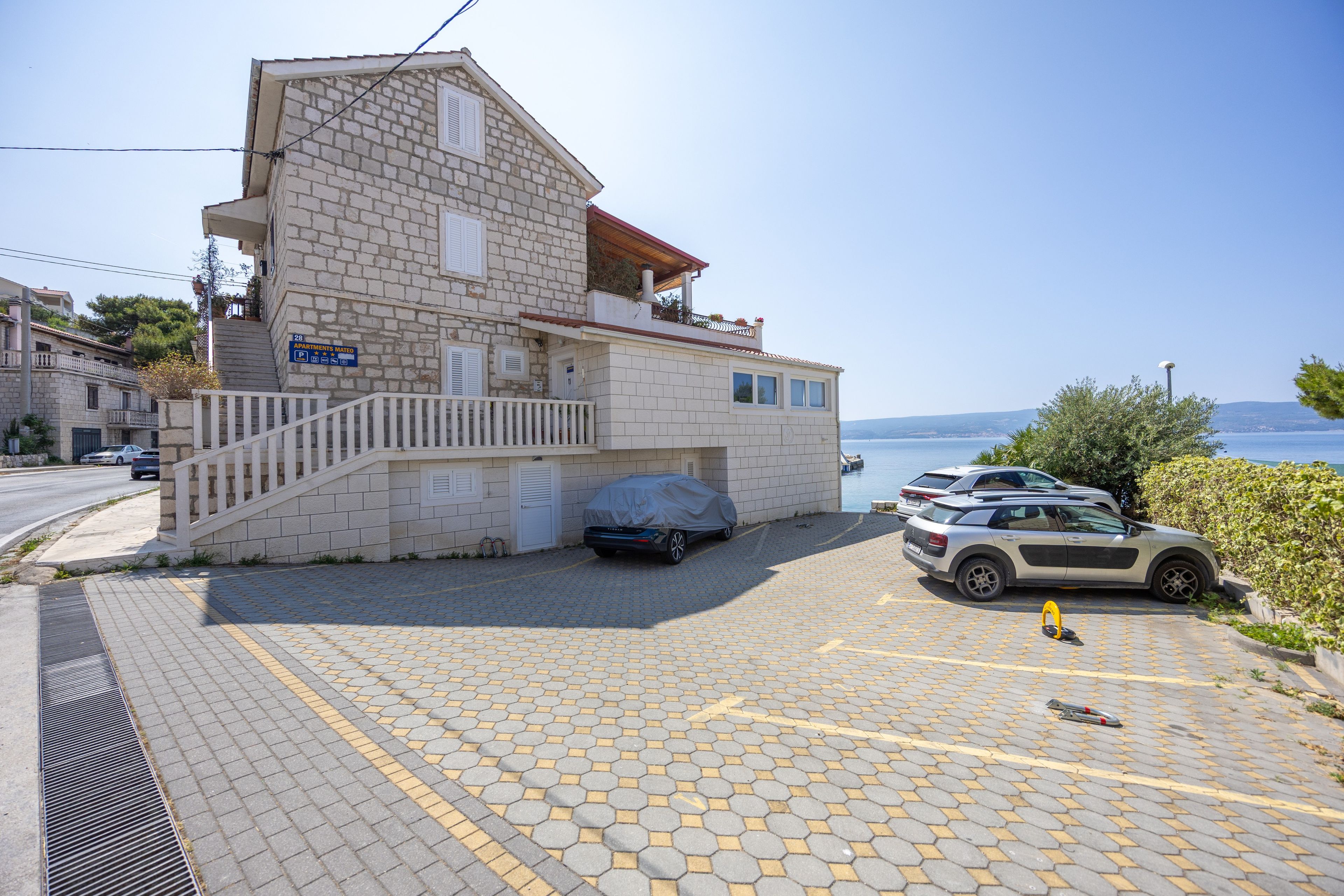 Un immeuble de deux étages avec une façade en pierre, un espace de stationnement couvert et une vue sur la mer.