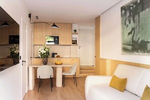 A modern kitchen with wooden cabinets, a dining area with a table and chairs, and a living room with a sofa and a painting on the wall. - Elegant A/C Apartment 1BR - 4P - Nation (Paris)