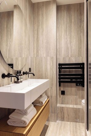 A modern bathroom with a white sink, black towel rack, and a glass shower enclosure. - Elegant A/C Apartment 1BR - 4P - Nation (Paris)