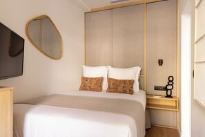 A hotel room with a bed, a bedside table, a mirror, and a wall-mounted TV. - Elegant A/C Apartment 1BR - 4P - Nation (Paris)