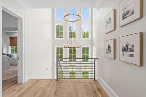 A spacious room with a wooden floor, a staircase with a metal railing, and large windows allowing natural light. - Private Pool, 4 King En-suites + Bunk Room, Outdoor Fireplace & Kitchen (Santa Rosa Beach)