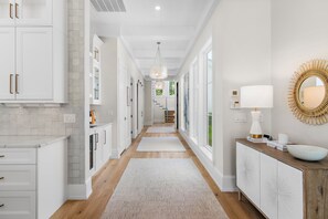 A hallway with white cabinetry, a wooden floor, a white rug, a chandelier, and a mirror with a sunburst design. - Private Pool, 4 King En-suites + Bunk Room, Outdoor Fireplace & Kitchen (Santa Rosa Beach)