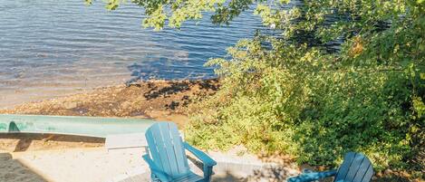 Een terras aan het meer met Adirondack-stoelen en een vuurkuil.