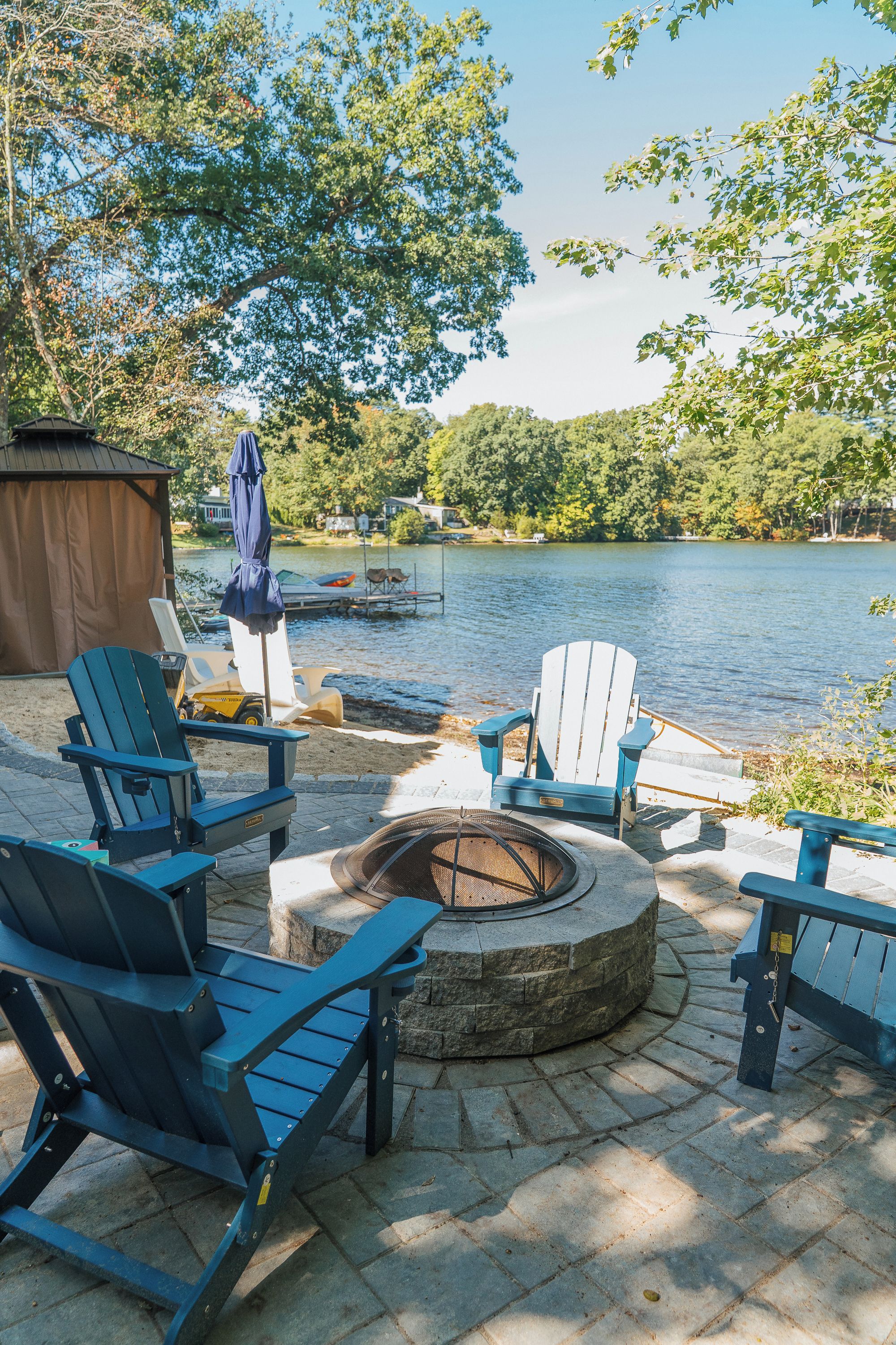 Un espacio al aire libre con sillas Adirondack, un brasero y vista a un lago.