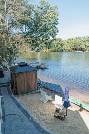 A lakeside property with a covered seating area, a boat dock, and a sandy beach.