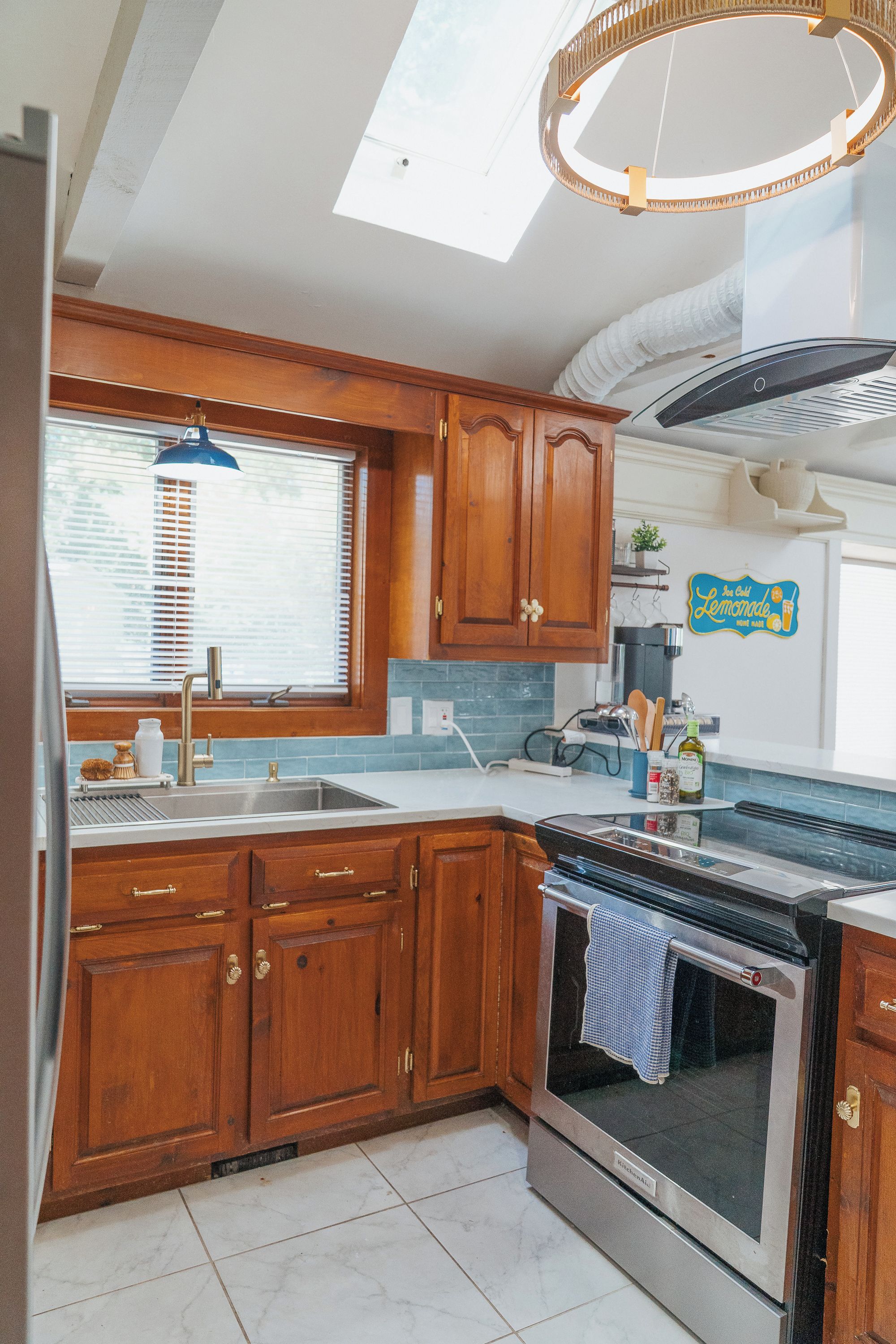 A kitchen with wooden cabinets, a built-in oven, a window with blinds, and a ceiling light fixture.