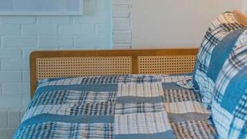 A bed with a checkered bedspread, a wooden headboard, and a wall-mounted light fixture.