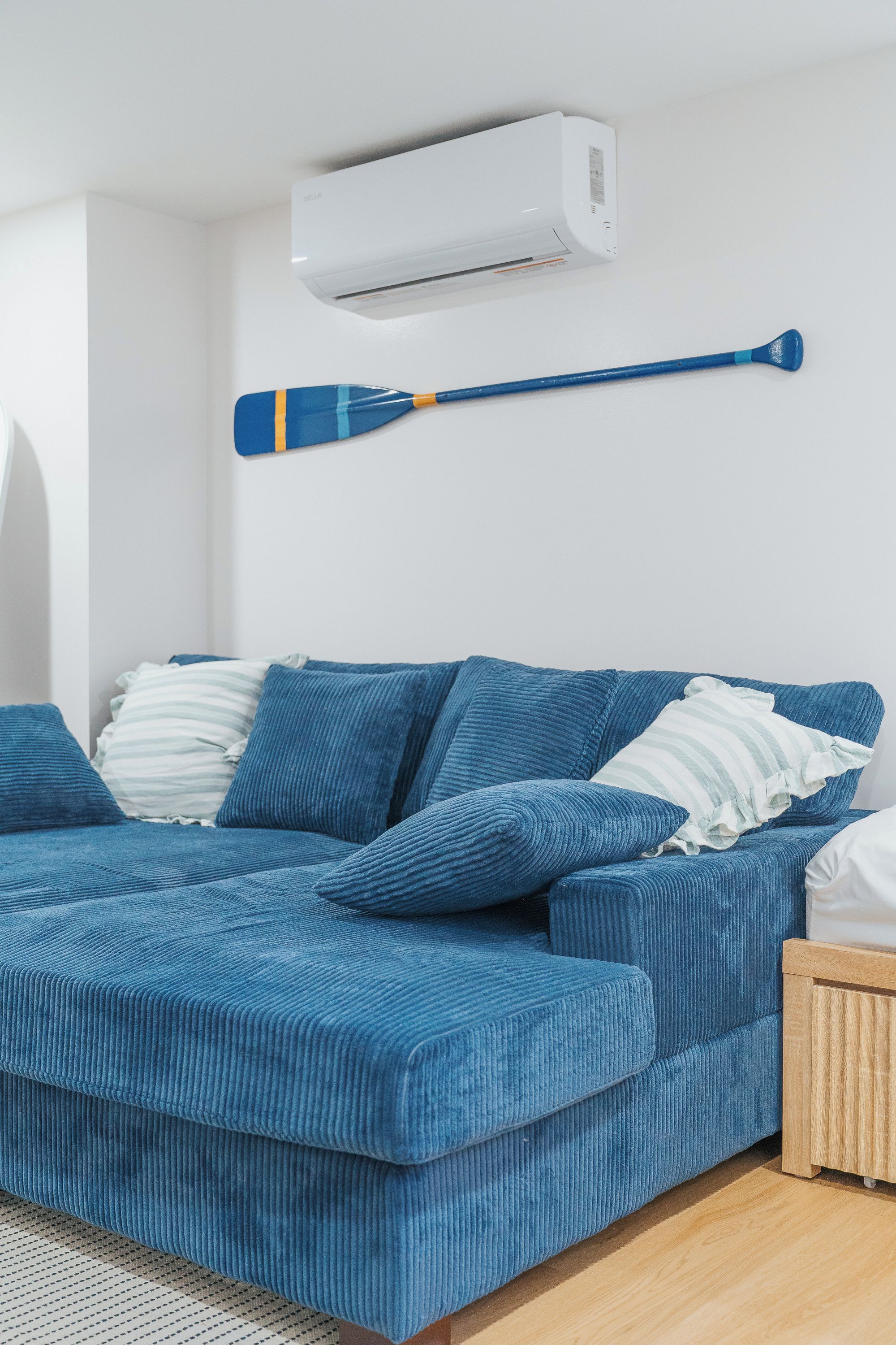 Une chambre moderne avec un canapé bleu, des coussins blancs et une pagaie bleue appuyée contre le mur.