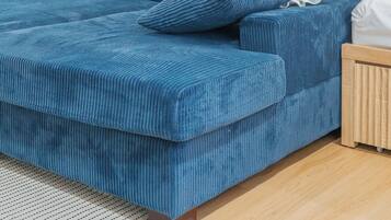 A modern bedroom with a blue sofa, white pillows, and a blue paddle leaning against the wall.