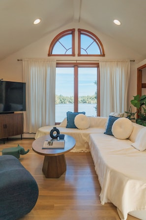 A cozy living room with a large arched window, a television, and a sofa with cushions.