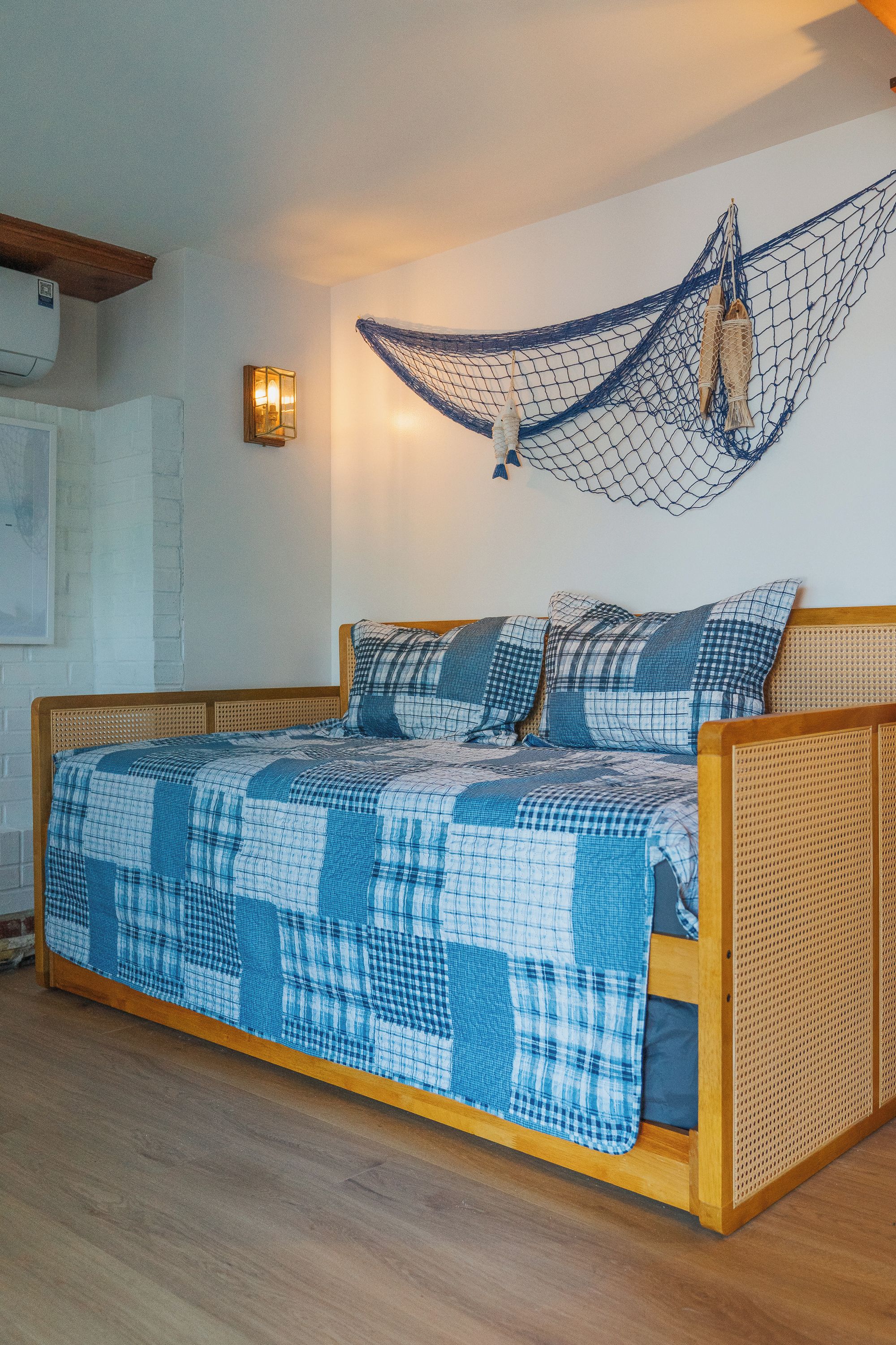 Un lit avec une couvre-lit à carreaux bleus et blancs, une tête de lit en bois et une décoration en forme de filet suspendu.