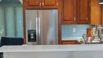 A modern kitchen with wooden cabinets, a stainless steel refrigerator, and a bar area with two stools.