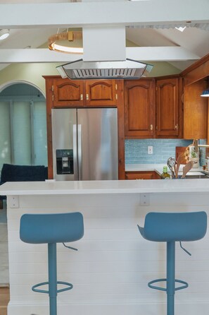 A modern kitchen with wooden cabinets, a stainless steel refrigerator, and a bar area with two stools.