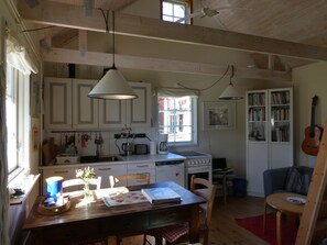A kitchen with white cabinets, a dining table with chairs, a coffee maker, and a guitar in the corner.