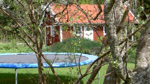 Um trampolim em uma área gramada, com árvores e um prédio de telhado vermelho ao fundo.