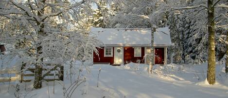 Een besneeuwde chalet met rode gevel, omringd door bomen en een houten hek.