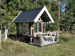 A wooden cabin with a metal roof, a deck with seating, and a sign indicating a location.