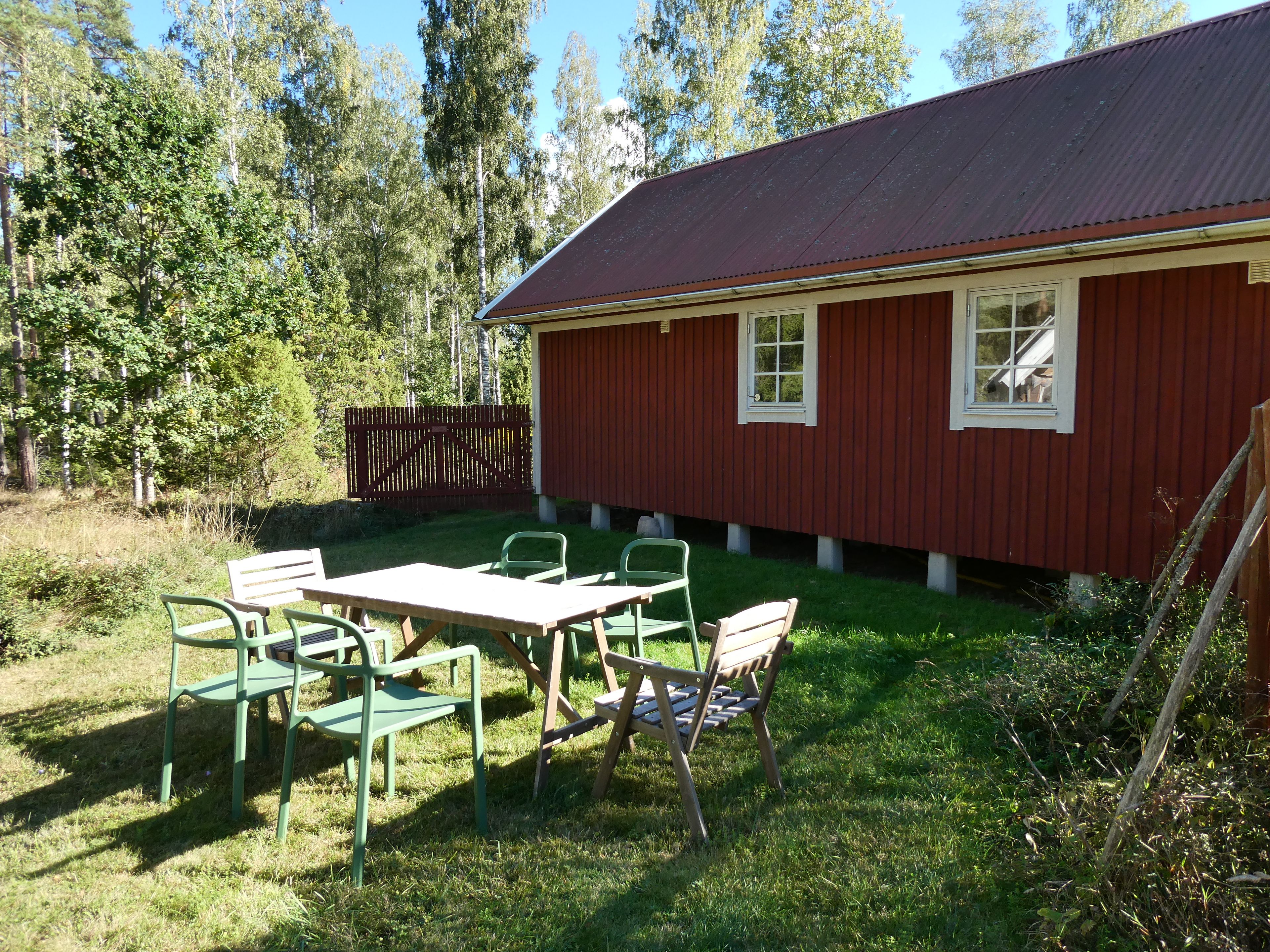 Un bâtiment rouge avec un toit en métal, une cour clôturée et une table entourée de chaises.