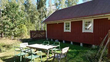 Un bâtiment rouge avec un toit en métal, une cour clôturée et une table entourée de chaises.
