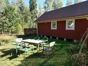 Een rood gebouw met een metalen dak, een omheind erf en een tafel met stoelen.